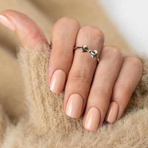 Graceful thin fingers of a girl with a trendy pastel nude manicure and a fluffy soft sweater and a cute silver ring bow