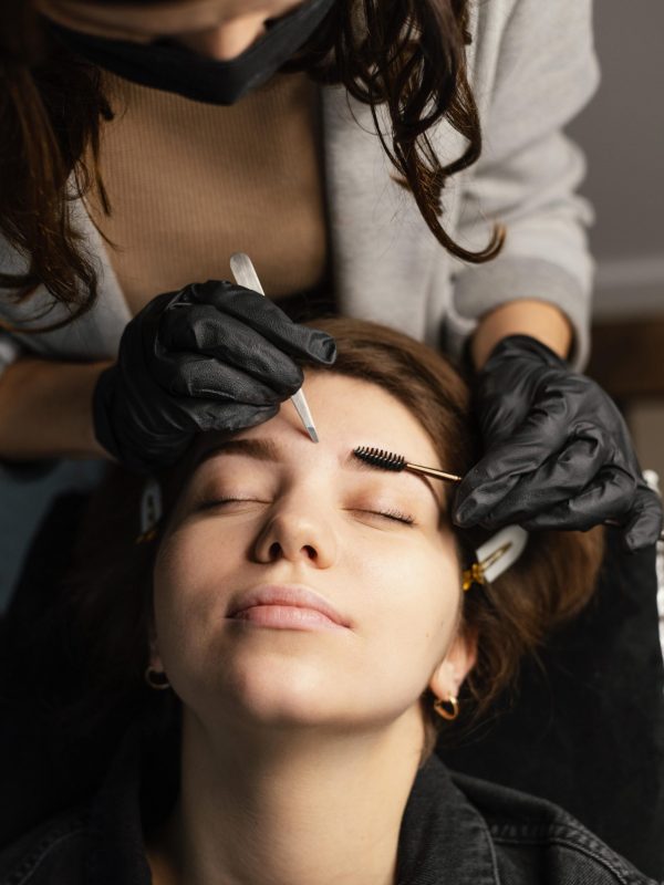 high-angle-female-clinician-doing-eyebrow-treatment-woman