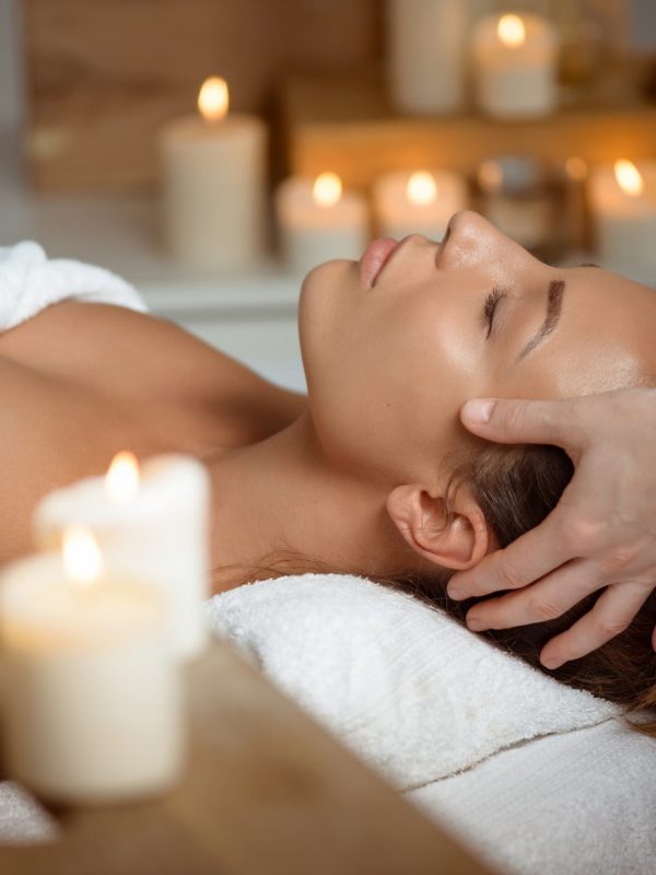Young beautiful brunette girl having face massage relaxing in spa salon. Eyes closed. Copy space.
